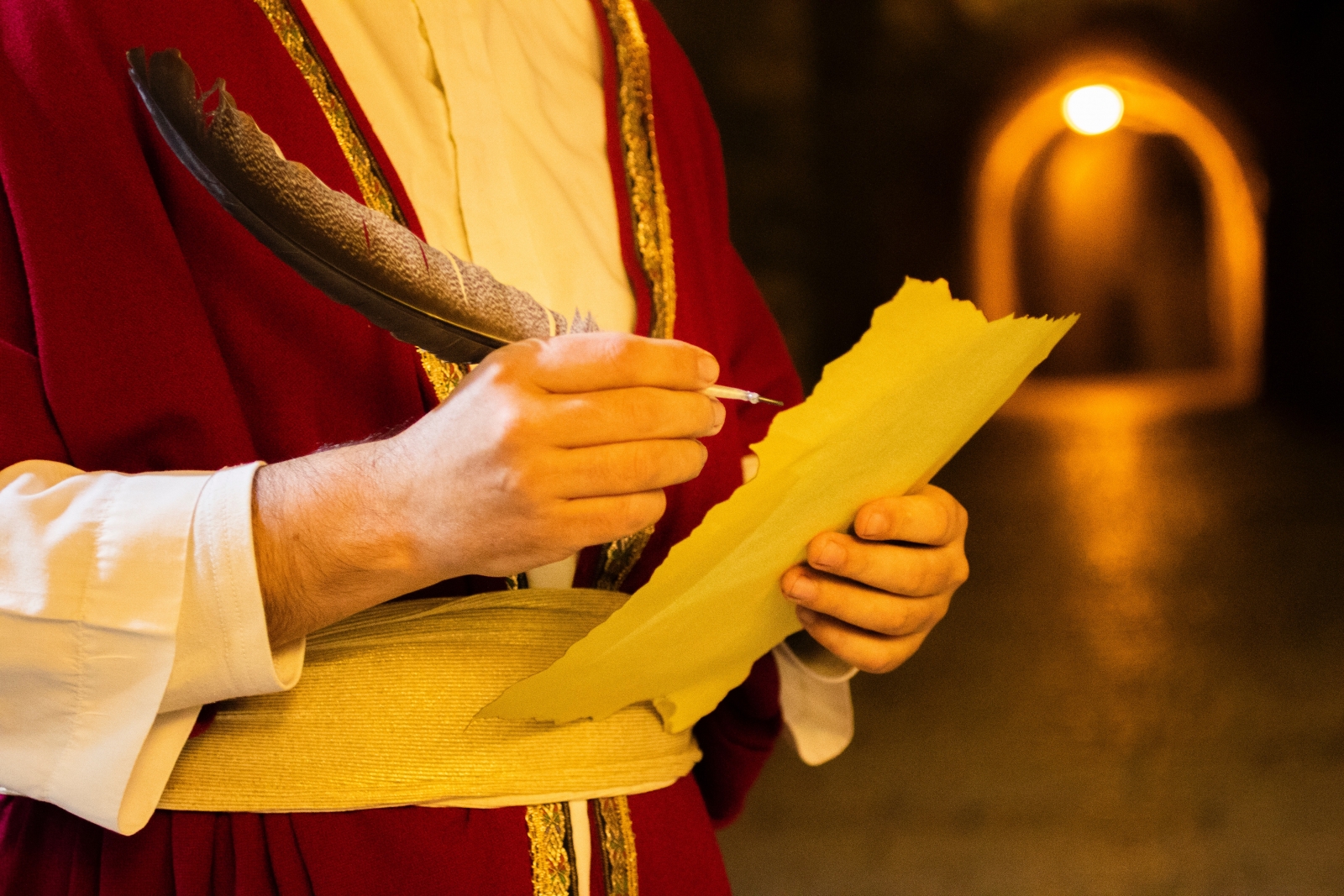 Mann in mittelalterlicher Tracht, schreibt mit Tinte und Feder auf ein Stück Papier.
