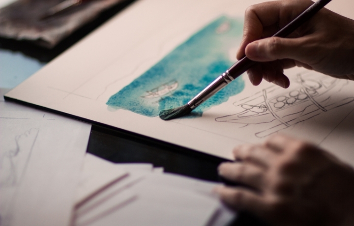 Zwei Hände, großes Blatt Papier. Blaues Aquarellbild entsteht.