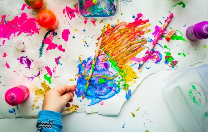 Kinderhand malt viele bunte Farbkleckse auf weißes Papier