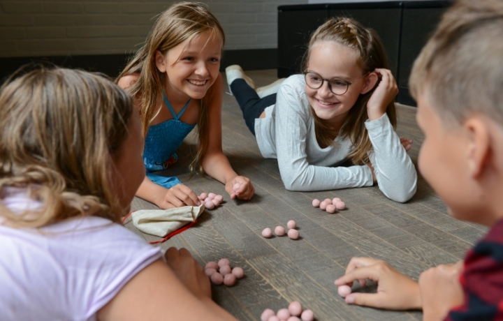 Vier Kinder spielen mit Murmeln auf dem Holzfußboden.