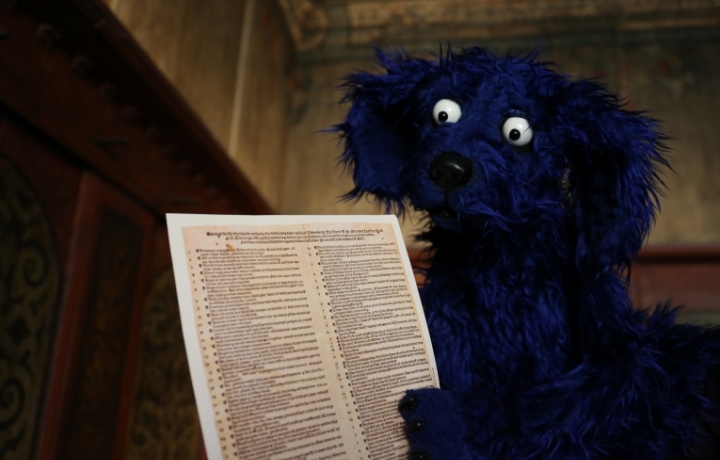 Handpuppe "blauer Hund" hält ein Schreiben in den Pfoten.