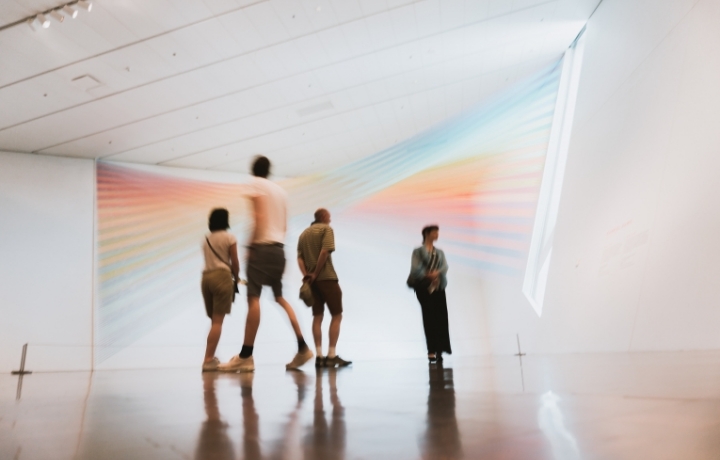 Vier Menschen stehen in einem weißen Raum, es soll ein Ausstellungsraum sein.