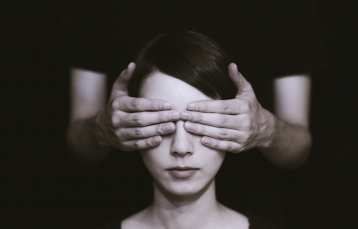Ein Frauengesicht im Fokus. Ein anderer Mensch, den man nicht sieht, hält der Frau die Augen zu.